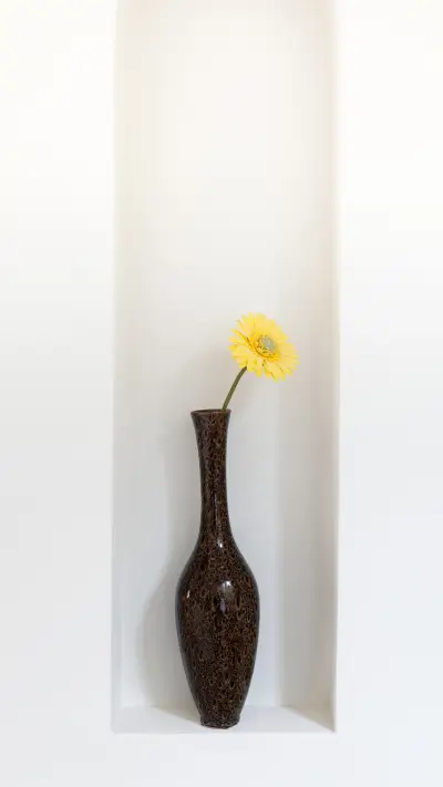 Vase with a single yellow flower displayed in a wall alcove