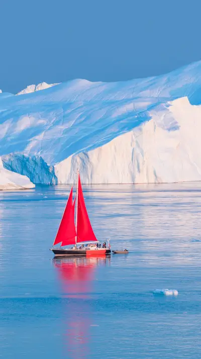 A red sailboat cruising among icebergs in Disko Bay
