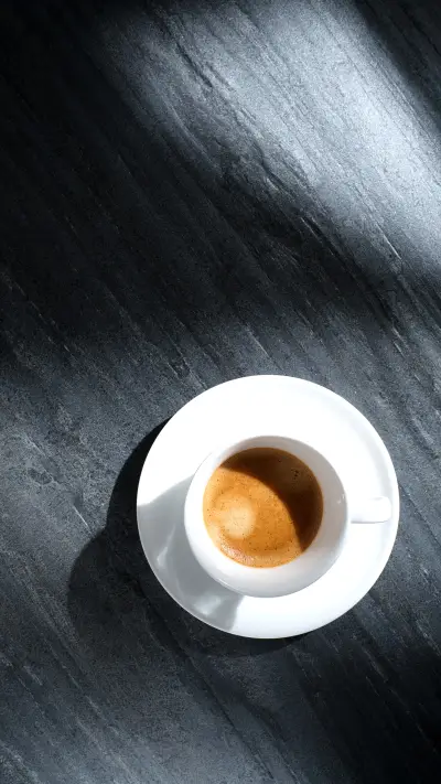White cup with coffee on a black textured stone table