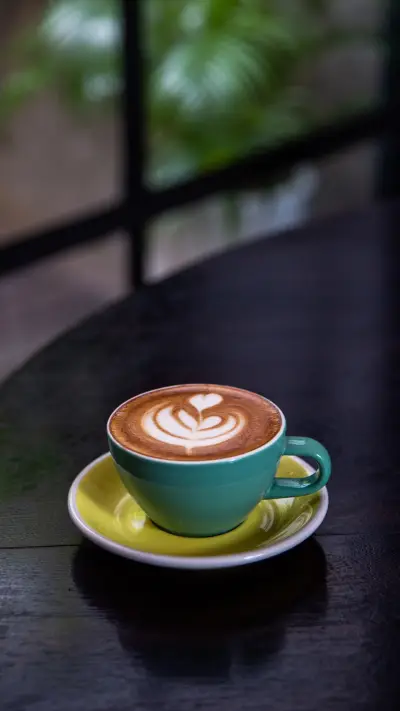 Green mug of cappuccino on wooden black background
